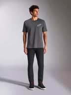 Alpinestars Angler CSF Tee, t-shirt z krótkim rękawem, antracytowy, z wyrazistym wielokolorowym logo Astars na piersi, prezentowany przez modela w czarnych spodniach i sneakersach, codzienna odzież streetwearowa w stylu motorsportowym