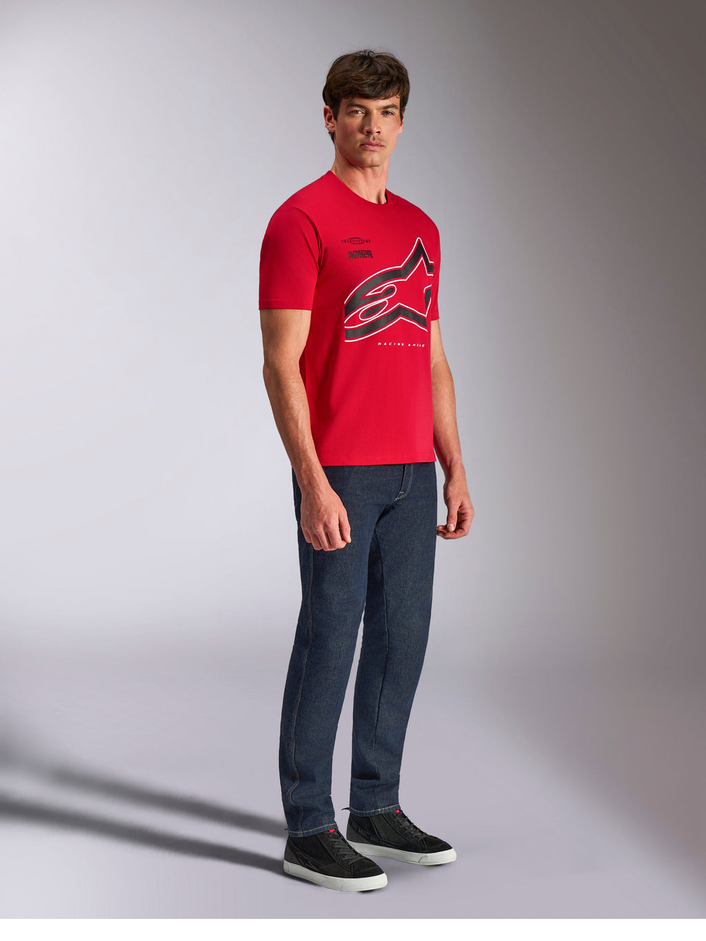 Alpinestars Authority CSF Tee, koszulka z krótkim rękawem, czerwona, duże przycięte logo Astars z czarnymi i białymi konturami, noszona przez modela z ciemnymi spodniami jeansowymi i czarnymi sneakersami, casualowy streetwear inspirowany sportami motorowymi