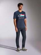Koszulka Alpinestars Trifecta CSF, t-shirt z krótkim rękawem, granatowa, z logo Astars, trójkolorowymi paskami i napisem „Racing Ahead”, noszona przez modela z ciemnymi dżinsami i sneakersami, codzienna odzież uliczna inspirowana sportami motorowymi