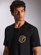 Alpinestars Aorbit CSF Tee, koszulka z krótkim rękawem, czarna, okrągła grafika na piersi Always Fast Made to Last z żółtym logo Astars, prezentowana przez modela, codzienna odzież motorsportowa typu streetwear