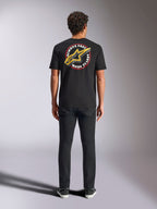 Alpinestars Aorbit CSF Tee, koszulka z krótkim rękawem, czarna, widok z tyłu na modelu w czarnych spodniach, z dużą grafiką „Always Fast Made to Last” i żółtym logo Astars, casualowa odzież uliczna w stylu motorsport