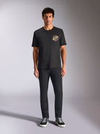 Alpinestars Aorbit CSF Tee, koszulka z krótkim rękawem, czarna, okrągłe logo z napisem „Always Fast Made to Last” na piersi, model w czarnych spodniach i sneakersach, codzienna odzież uliczna inspirowana sportami motorowymi