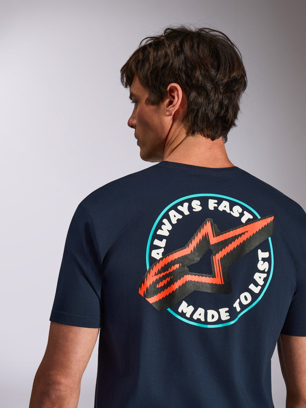 Alpinestars Aorbit CSF Tee, granatowa koszulka z krótkim rękawem, widok z tyłu z grafiką Always Fast Made to Last i pomarańczowym logo gwiazdy, casualowa odzież motorsportowa