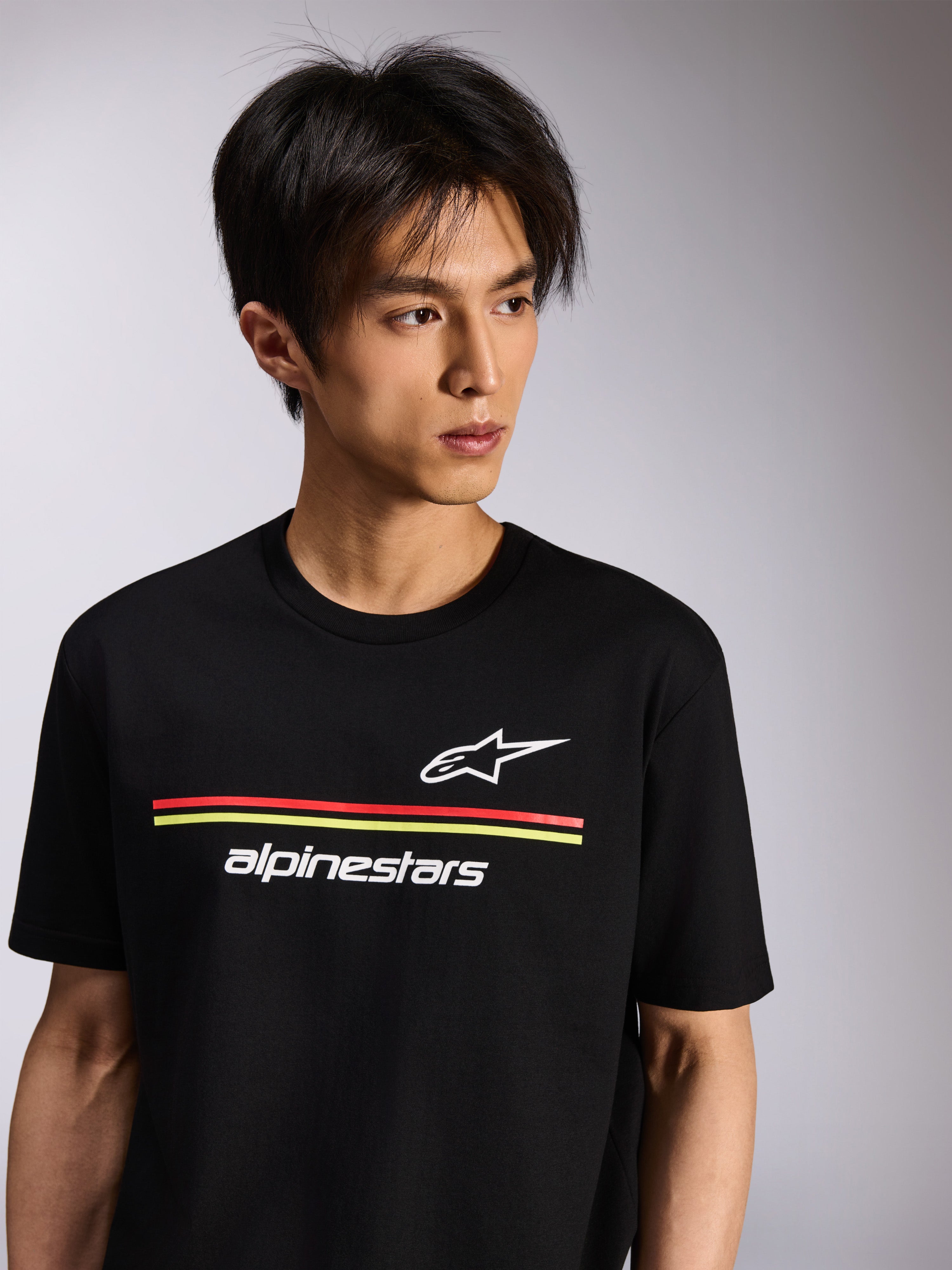 Alpinestars Lanes CSF Tee, koszulka z krótkim rękawem, czarna, z białym logo Astars i Alpinestars oraz czerwonymi i żółtymi paskami, casualowy motorsport streetwear prezentowany na modelu