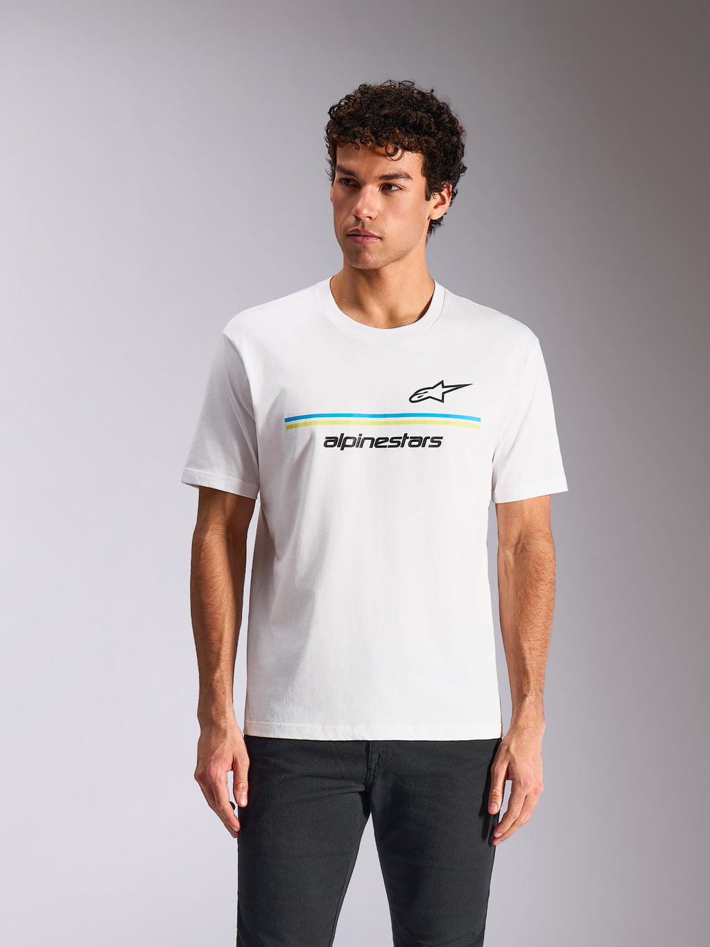 Alpinestars Lanes CSF Tee, biała koszulka z krótkim rękawem, czarne logo Astars nad niebieskimi i limonkowymi poziomymi pasami oraz napis „alpinestars”, prezentowana na modelu, codzienna odzież streetwearowa w stylu motorsport