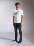 Alpinestars Lanes CSF Tee, biała koszulka z krótkim rękawem, model w czarnych spodniach slim-fit i czarnych wysokich sneakersach, z niebieskimi i żółtymi poziomymi paskami oraz logo Alpinestars na piersi, codzienna odzież streetwearowa inspirowana sportami motorowymi