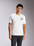 Alpinestars Order CSF Tee, koszulka z krótkim rękawem, biała, grafika na piersi z kaskiem i palmami, noszona przez modela do ciemnych spodni, casualowy streetwear inspirowany motorsportem