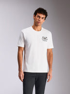 Alpinestars Order CSF Tee, koszulka z krótkim rękawem, biała, grafika na piersi z kaskiem i palmami, noszona przez modela do ciemnych spodni, casualowy streetwear inspirowany motorsportem