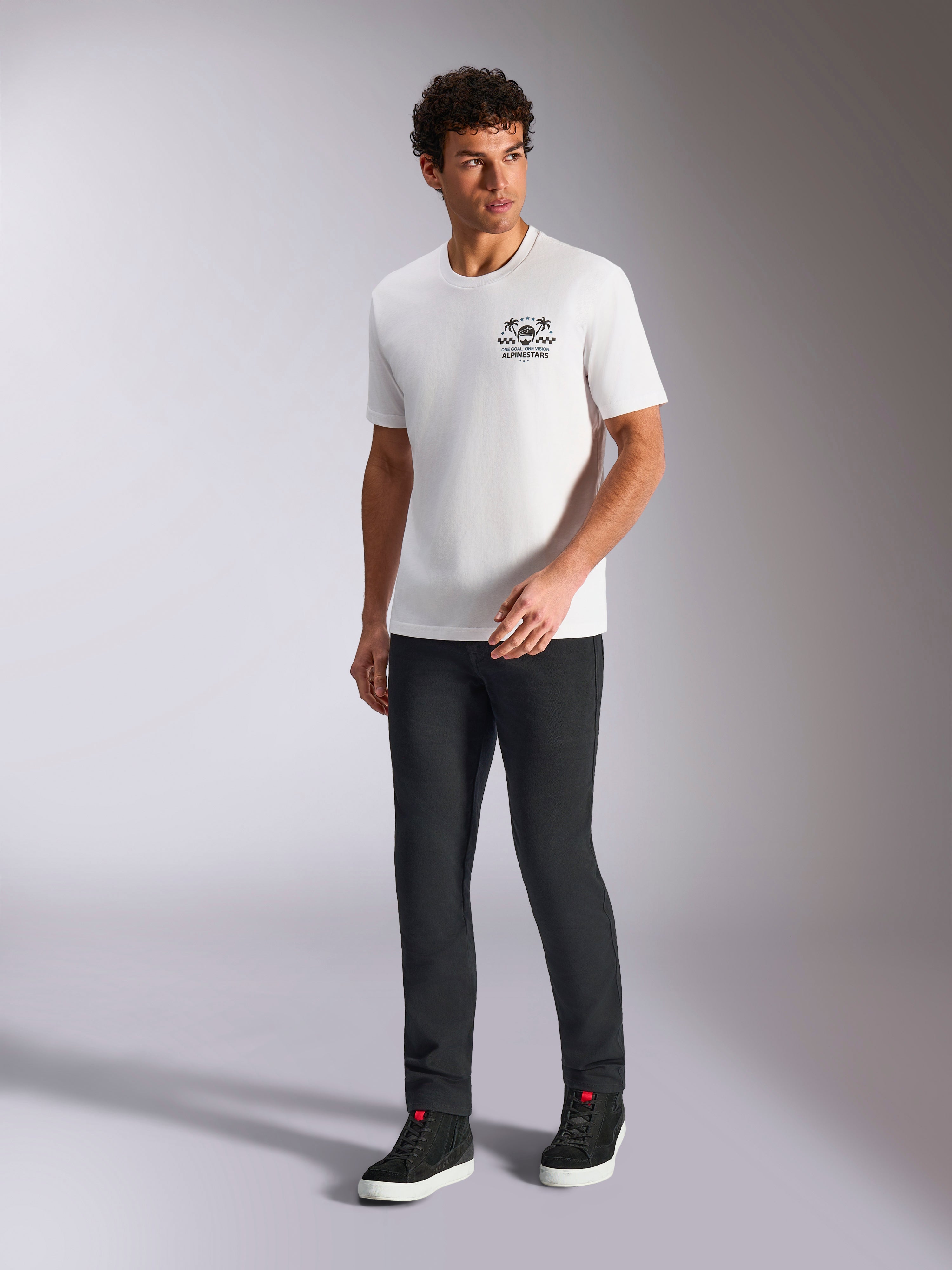 Alpinestars Order CSF Tee, biała koszulka z krótkim rękawem, logo z kaskiem i palmami, noszona z czarnymi spodniami i wysokimi sneakersami, casualowa odzież uliczna w stylu motorsport