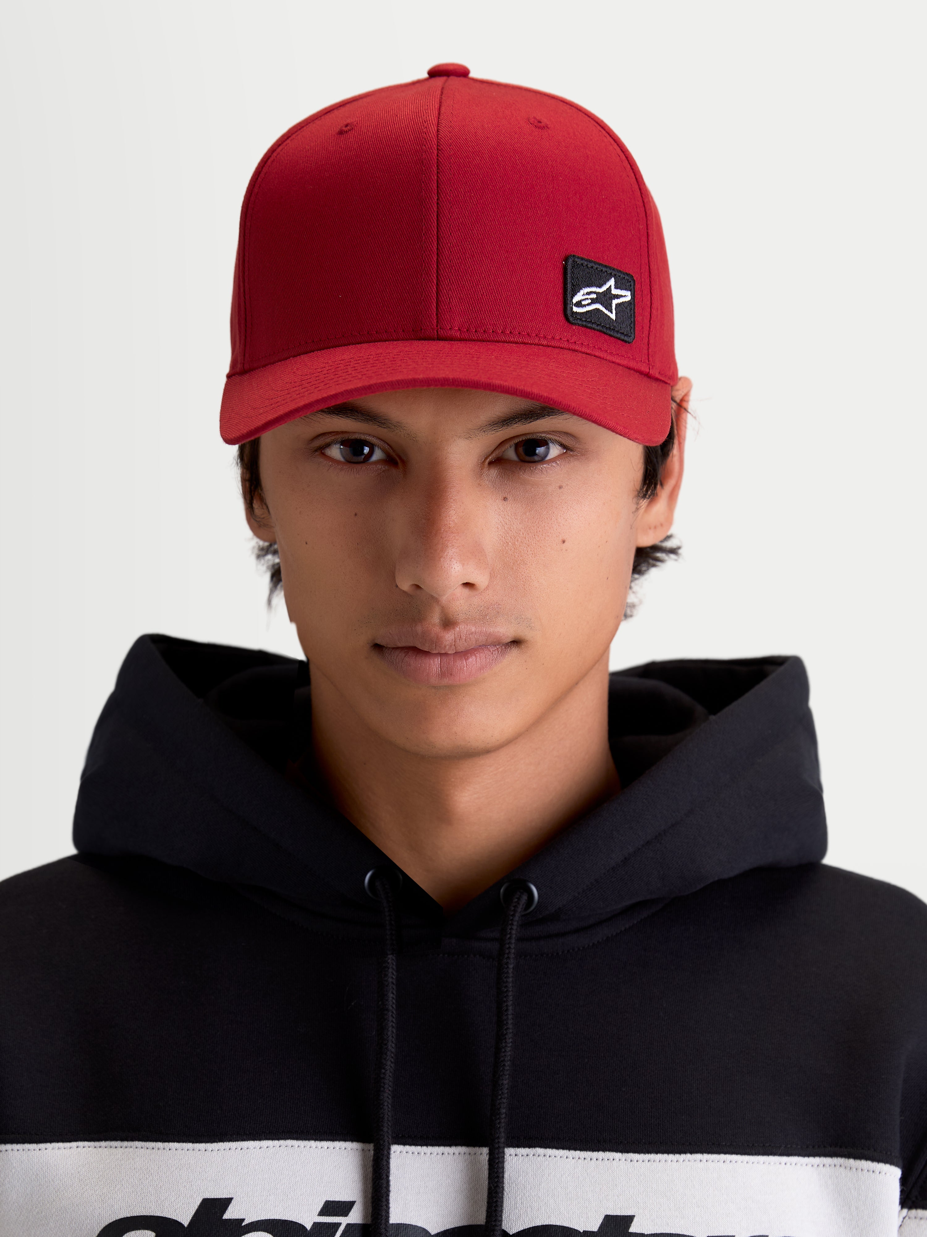 Alpinestars Czapka Pivot, ciemnoczerwona czapka z daszkiem sportswear, unisex, widok z przodu na modelu, haftowana naszywka z logo Astars, zakrzywiony daszek, usztywniona korona i trwała konstrukcja z kepru.