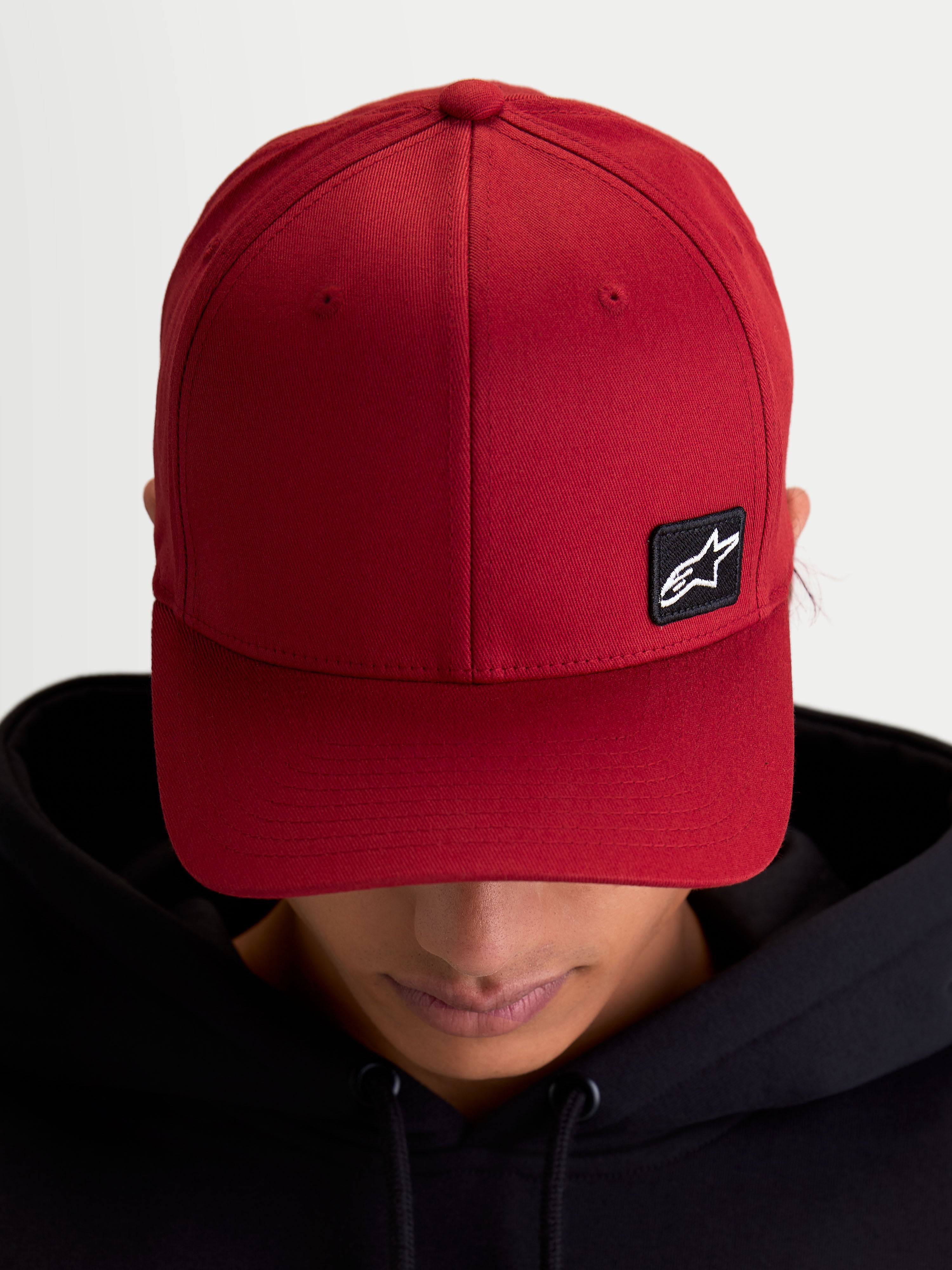 Alpinestars czapka Pivot, sportowa czapka z daszkiem typu baseball cap, ciemnoczerwona, unisex, zakrzywiony daszek i usztywniona korona, mała czarna haftowana naszywka z logo Astars na trwałej tkaninie keprowej, widok na modelu.