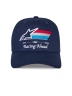 Alpinestars Trifecta Snapback Hat, granatowa czapka z zakrzywionym daszkiem, haftowane logo z przodu z białą gwiazdą i trójkolorowymi paskami, białe napisy „Racing Ahead” i „Goal One Vision”, usztywniona korona, codzienne nakrycie głowy inspirowane motorsportem