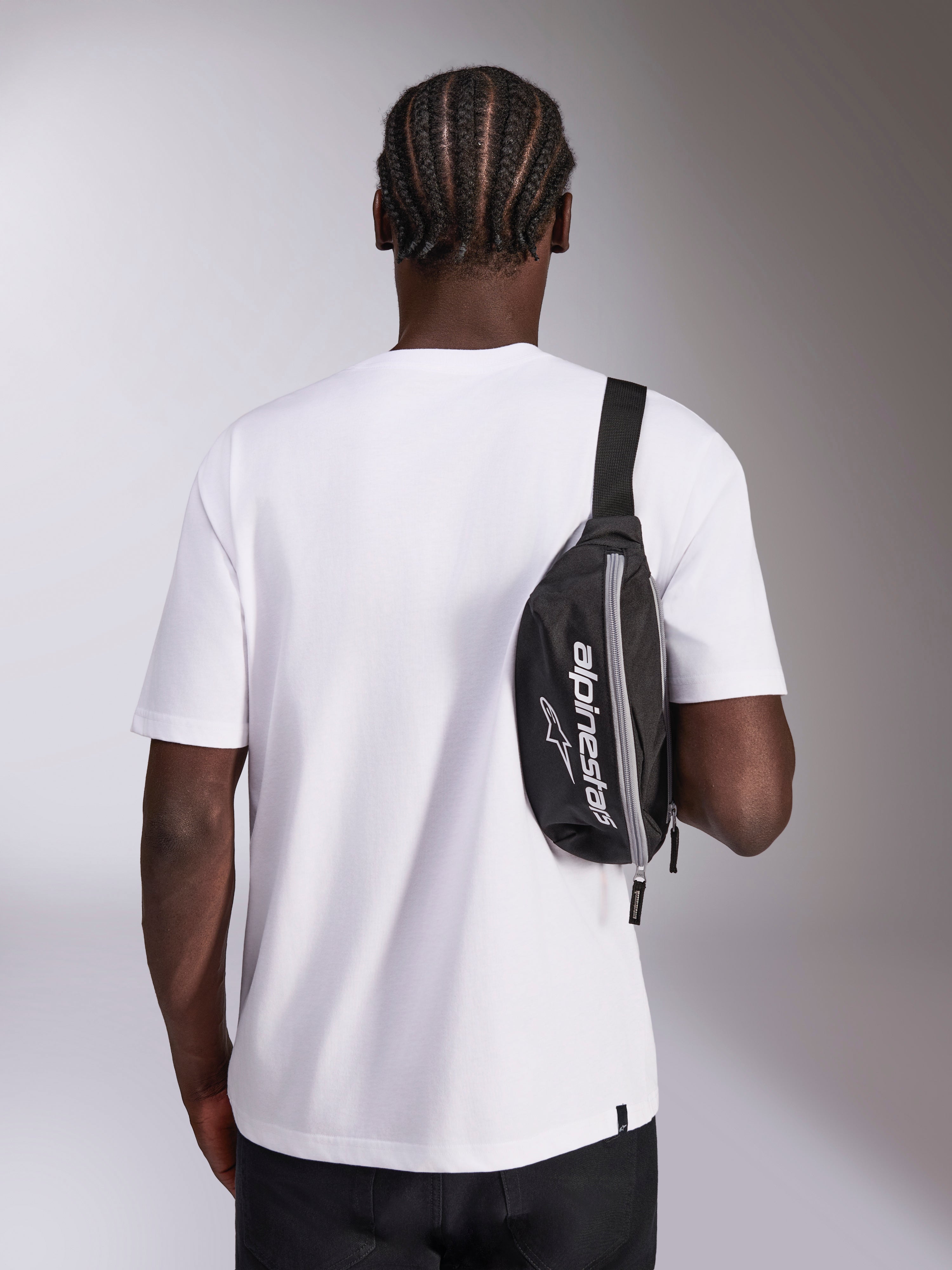 Alpinestars Only Linear Hip Bag, czarna nerka z białym logo Alpinestars, noszona jako torba crossbody na białym t-shircie, codzienny dodatek streetwearowy inspirowany sportami motorowymi