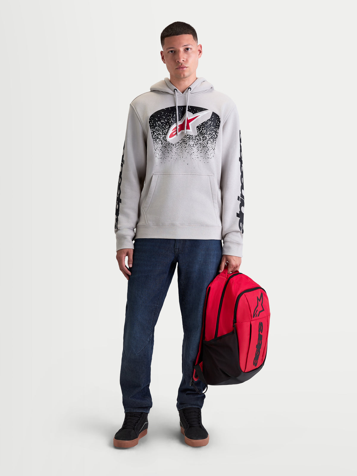 Alpinestars GFX Boss, czerwony i czarny plecak miejski o pojemności 20l, wykonany z wytrzymałego poliestru 600D z wypukłym silikonowym logo Astars, trzymany przez mężczyznę, akcesoria sportowe.
