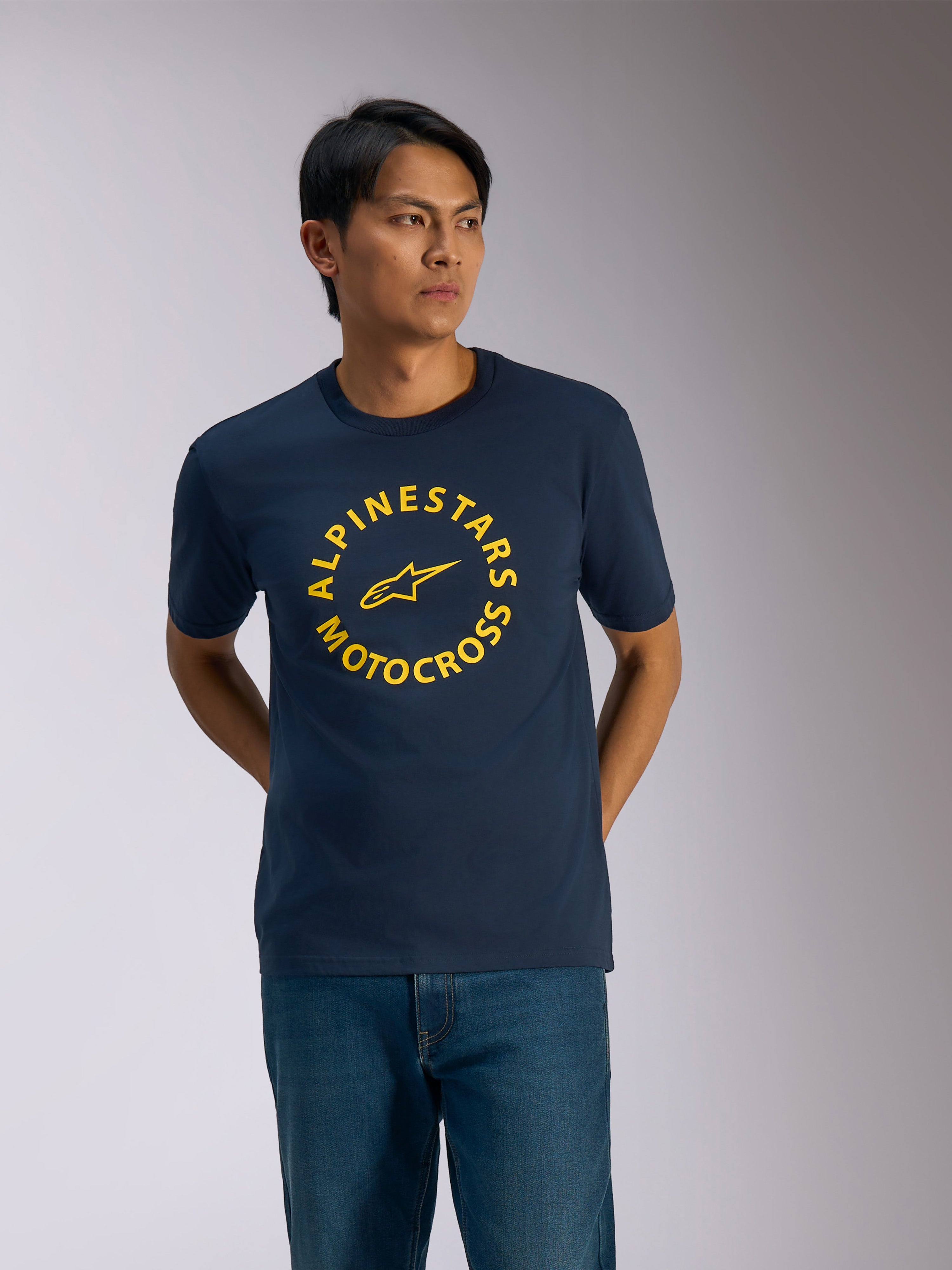 Alpinestars MX CSF Tee, T-shirt z krótkim rękawem, granatowy, żółta okrągła grafika Alpinestars Motocross z logo gwiazdy w środku, noszona przez mężczyznę do niebieskich jeansów, casualowa odzież streetwearowa w stylu motorsportowym