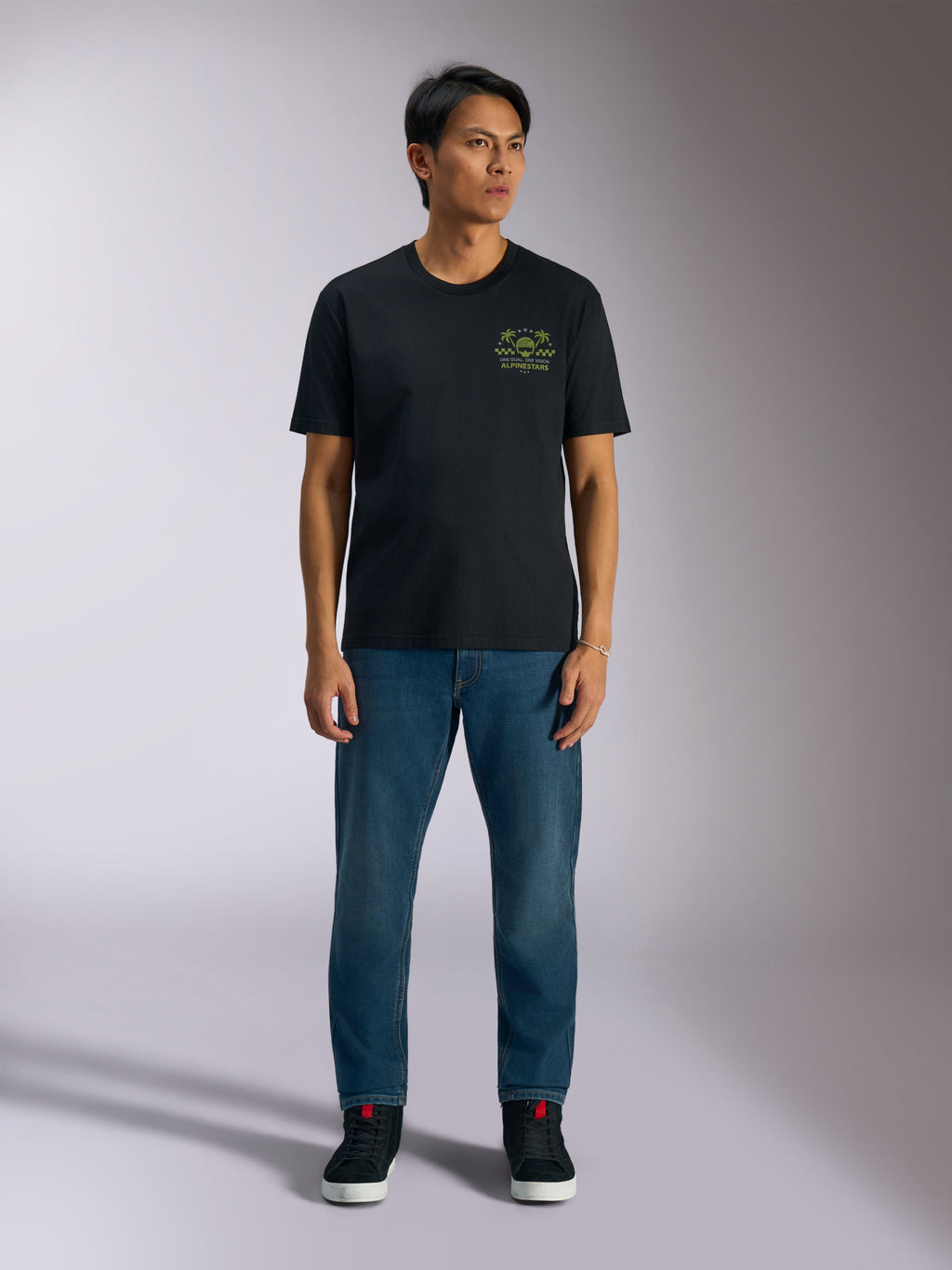 Alpinestars Order CSF Tee, czarna koszulka z krótkim rękawem, limonkowa grafika z kaskiem i palmami na piersi, zestawiona z niebieskimi jeansami i czarnymi sneakersami, codzienna odzież motorsportowa