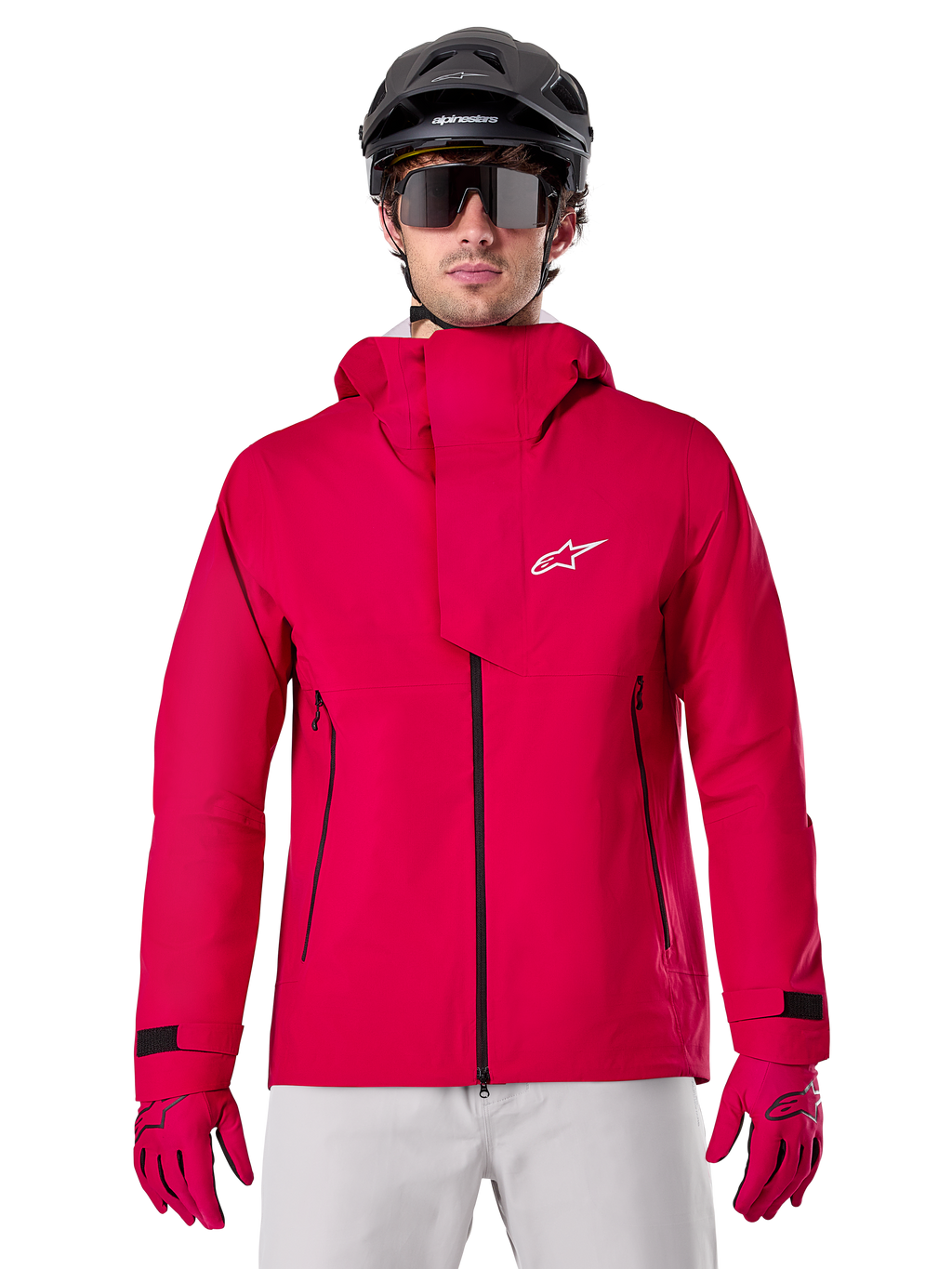 Alpinestars A-Dura Elite Waterproof Jacket, kurtka przeciwdeszczowa MTB, czerwony fluo, wysoki kołnierz z białym logo Alpinestars, czarne detale zamków, noszona z pasującymi rękawicami i czarnym kaskiem rowerowym, techniczna wodoodporna odzież rowerowa