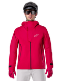 Alpinestars A-Dura Elite Waterproof Jacket, kurtka przeciwdeszczowa MTB, czerwony fluo, wysoki kołnierz z białym logo Alpinestars, czarne detale zamków, noszona z pasującymi rękawicami i czarnym kaskiem rowerowym, techniczna wodoodporna odzież rowerowa