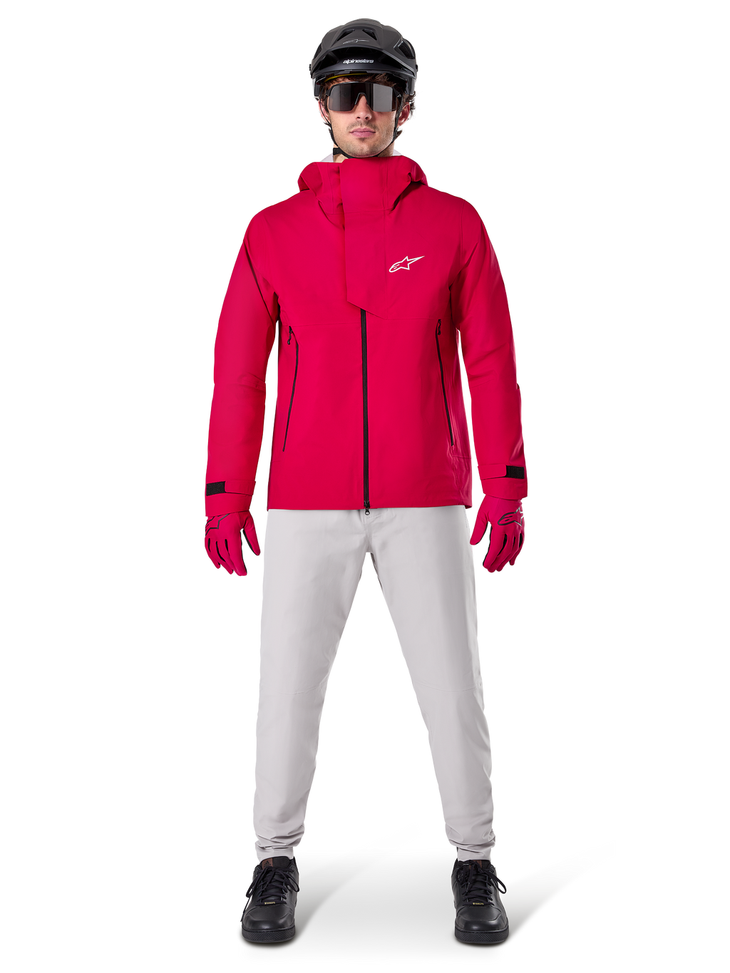 Wodoodporna kurtka Alpinestars A-Dura Elite, Red Fluo, techniczna kurtka rowerowa MTB noszona z czarnym kaskiem MTB, okularami przeciwsłonecznymi, pasującymi czerwonymi rękawiczkami i jasnoszarymi spodniami, widok całej sylwetki w odzieży rowerowej na każdą pogodę