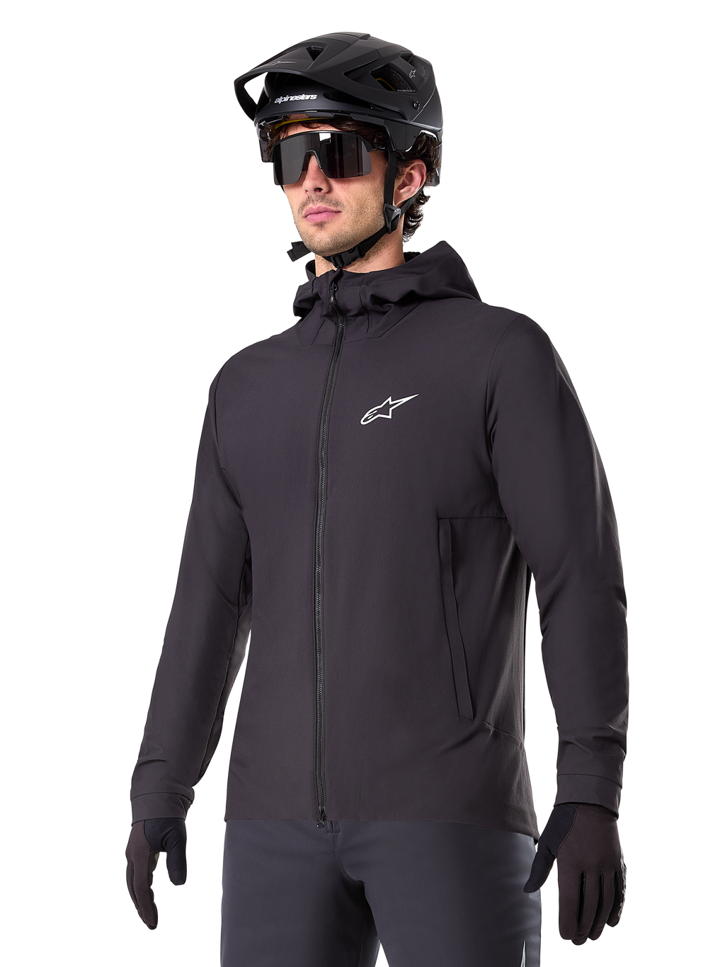 Alpinestars A-Dura Thermal Jacket, czarna kurtka rowerowa, fason z kapturem i zamkiem błyskawicznym z przodu, białe logo z gwiazdą na piersi, noszona z czarnym kaskiem MTB i rękawiczkami, sportowa odzież wyczynowa do jazdy na szlaku w zimne dni