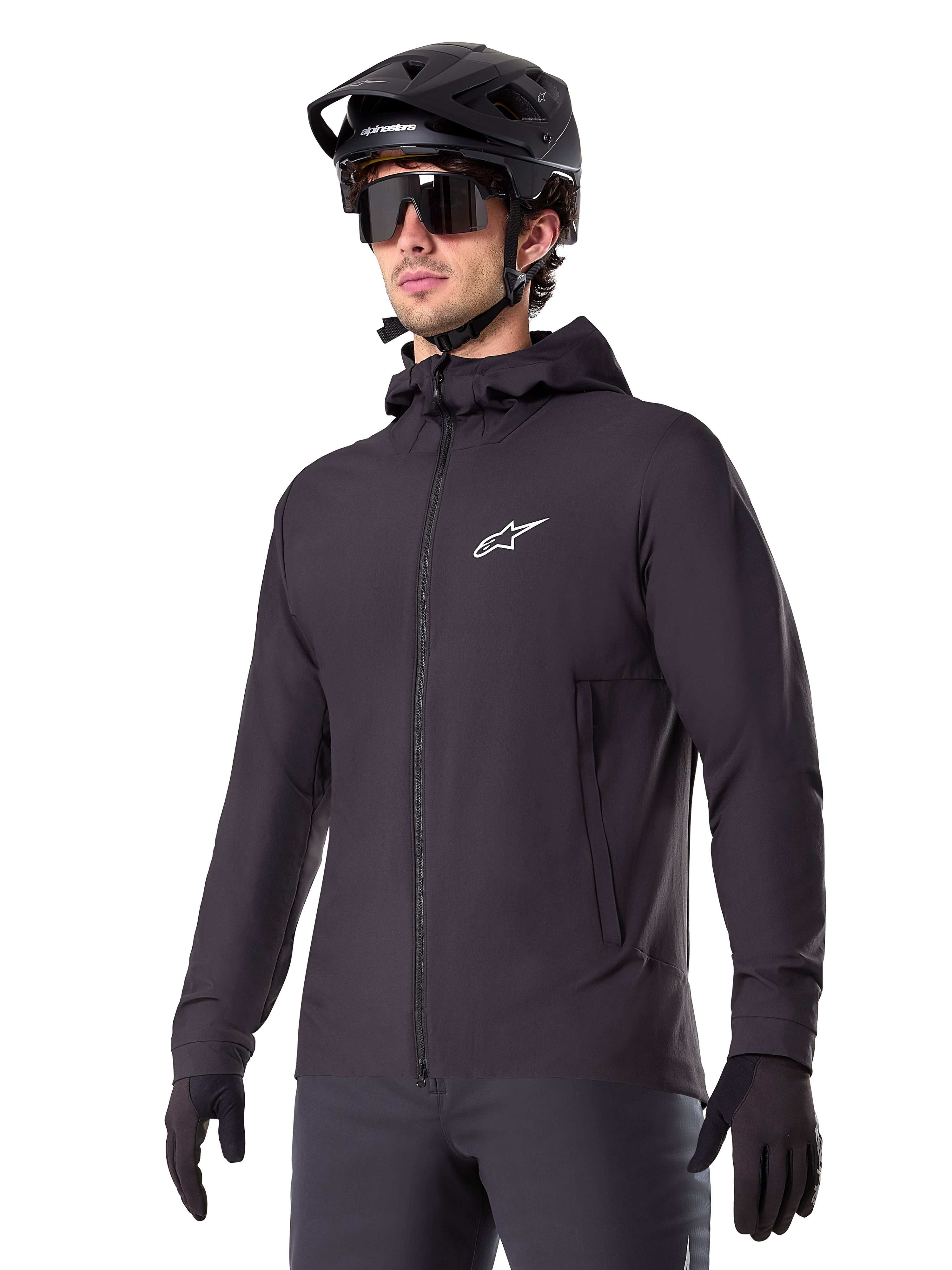 Alpinestars A-Dura Thermal Jacket, czarna kurtka rowerowa, fason z kapturem i zamkiem błyskawicznym z przodu, białe logo z gwiazdą na piersi, noszona z czarnym kaskiem MTB i rękawiczkami, sportowa odzież wyczynowa do jazdy na szlaku w zimne dni