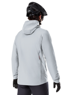 Kurtka Alpinestars A-Dura Thermal, Titanium Gray, widok od tyłu rowerzysty w ocieplanej kurtce z kapturem, w zestawieniu z czarnym kaskiem MTB i czarnymi rękawiczkami, małe logo Alpinestars na dole pleców, zaprojektowana do jazdy MTB w niskich temperaturach