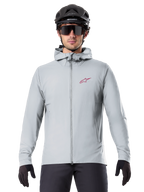 Alpinestars A-Dura Thermal Jacket w kolorze Titanium, jasnoszara kurtka rowerowa z kapturem i czerwonym logo gwiazdy na piersi, noszona przez rowerzystę w czarnym kasku MTB, okularach i rękawiczkach, ocieplana odzież do kolarstwa górskiego