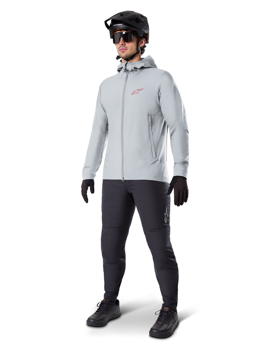 Alpinestars A-Dura Thermal Jacket w kolorze Titanium, jasnoszara rowerowa kurtka z kapturem z czerwonym logo Alpinestars na piersi, noszona przez mężczyznę w czarnym kasku MTB, okularach przeciwsłonecznych, ciemnoszarych spodniach i czarnych rękawiczkach, profesjonalny sprzęt MTB