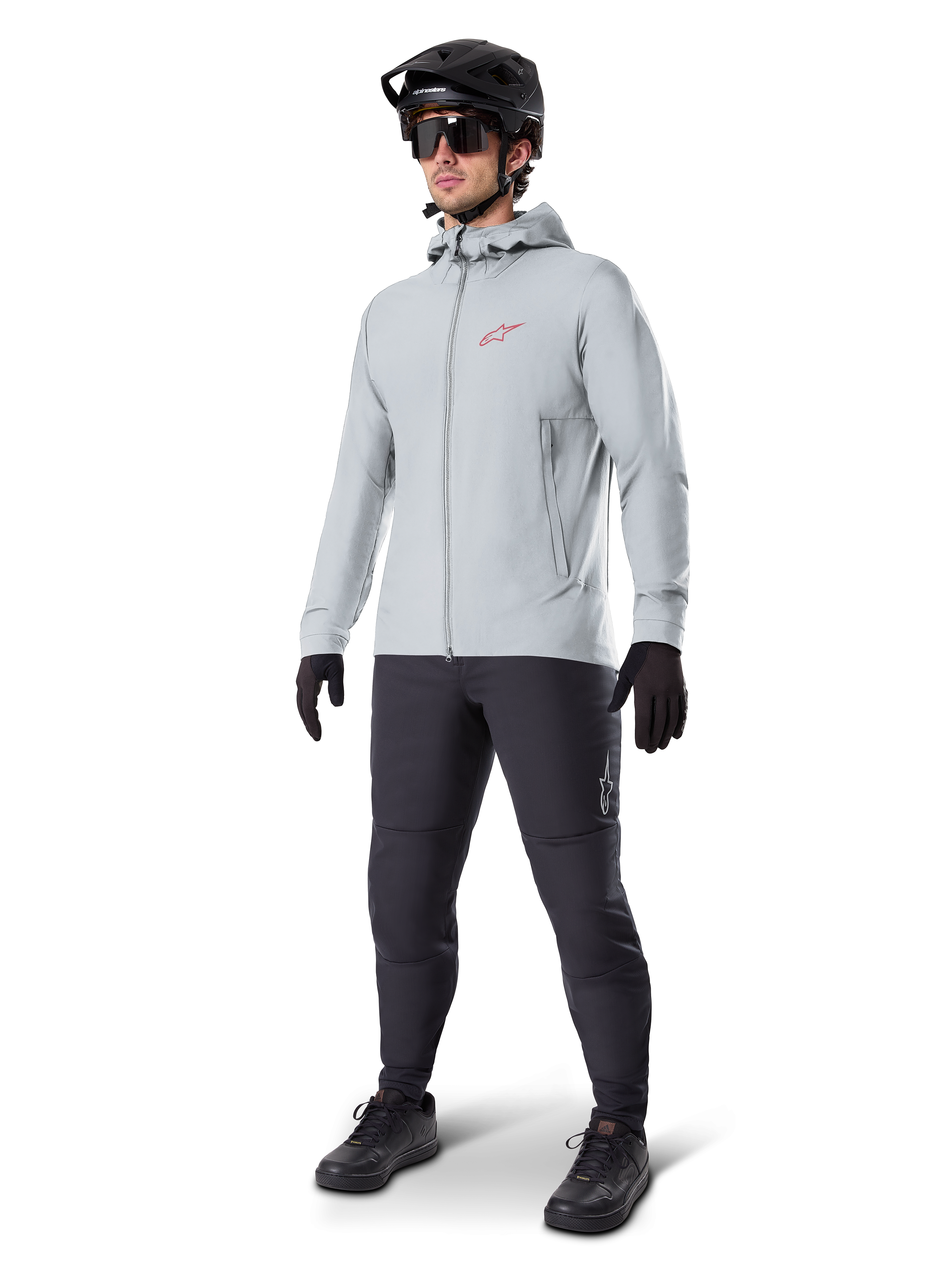 Alpinestars A-Dura Thermal Jacket w kolorze Titanium, jasnoszara rowerowa kurtka z kapturem z czerwonym logo Alpinestars na piersi, noszona przez mężczyznę w czarnym kasku MTB, okularach przeciwsłonecznych, ciemnoszarych spodniach i czarnych rękawiczkach, profesjonalny sprzęt MTB