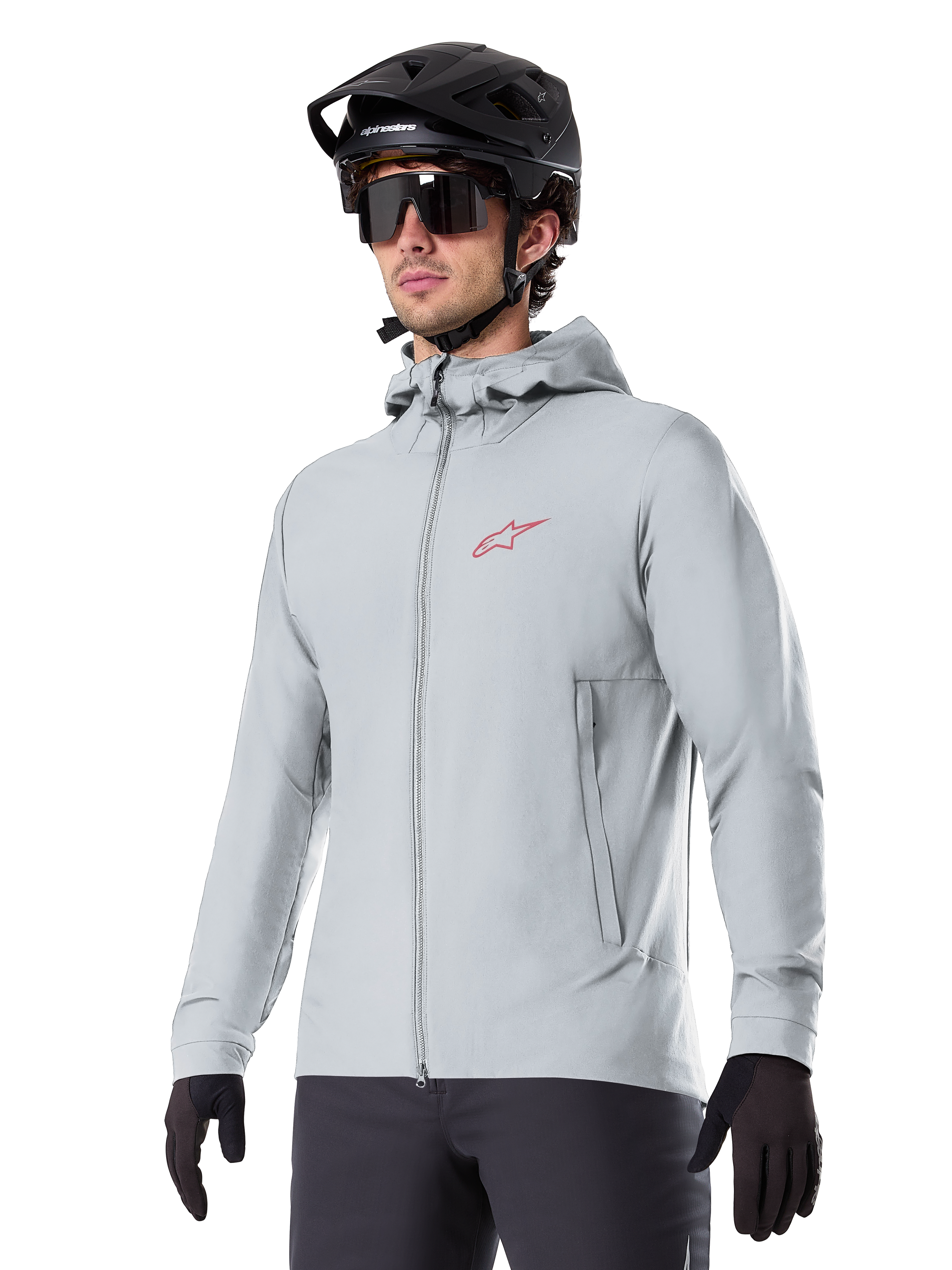 Alpinestars A-Dura Thermal Jacket, jasnoszara ocieplana kurtka rowerowa, model z kapturem i małym czerwonym logo, noszona z czarnym kaskiem i rękawiczkami, techniczna odzież na rower górski do jazdy w niskich temperaturach