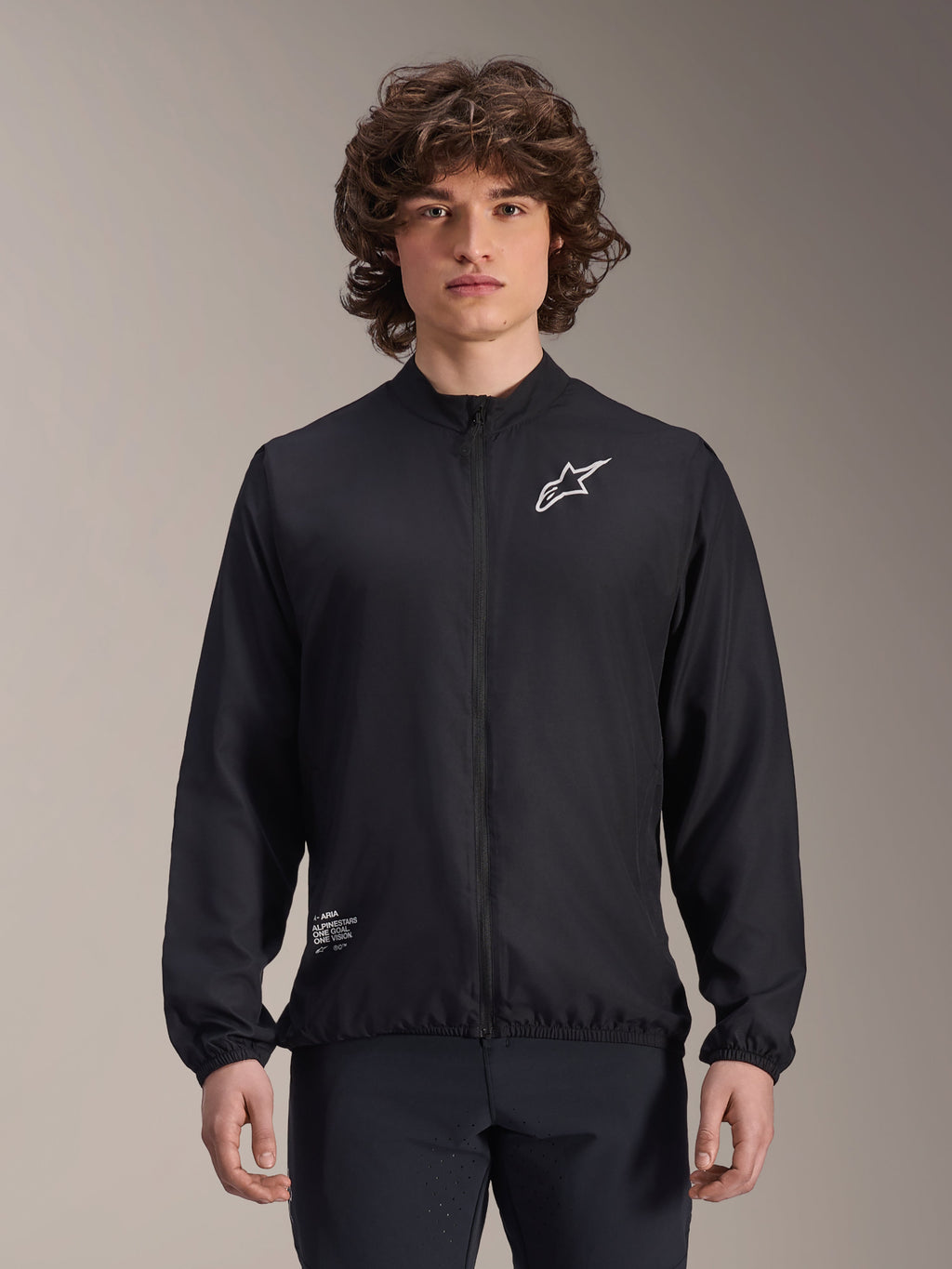 Alpinestars A-Aria Windbreaker Jacket, czarna, lekka kurtka rowerowa typu wiatrówka, z białym logo Astars na klatce piersiowej i brandingiem na dole po prawej stronie, pełny zamek, stójka, elastyczne mankiety i dolny brzeg, sportowy krój do aktywności na zewnątrz