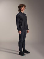 Alpinestars A-Aria Windbreaker Jacket, czarna, lekka wiatroodporna kurtka rowerowa noszona przez modela z kręconymi włosami, z białym logo Astars na piersi i brandingiem na dole po prawej stronie, zestawiona z czarnymi spodniami i butami, sportowy krój idealny do jazdy MTB i gravelowej