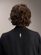 Kurtka Alpinestars A-Aria Windbreaker, czarna, zbliżenie z tyłu na górną część ramion i kołnierz, małe białe logo na środku pleców, model z brązowymi falowanymi włosami, minimalistyczna wyczynowa odzież rowerowa