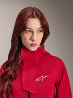 Alpinestars Stella A-Dura Elite Waterproof Jacket, Red Fluo, noszona przez kobietę z długimi rudymi włosami, techniczna 3-warstwowa wodoodporna kurtka z wysokim kołnierzem i białym logo, odzież outdoorowa i rowerowa MTB o wysokiej wydajności