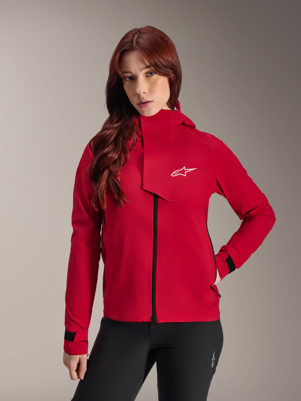 Alpinestars Stella A-Dura Elite Waterproof Jacket, damska kurtka rowerowa MTB, jaskrawoczerwona (Red Fluo), z przednią klapą przeciwdeszczową z białym logo Alpinestars, wysokim kołnierzem i regulowanymi mankietami, zestawiona z czarnymi spodniami dla technicznego kolarskiego wyglądu