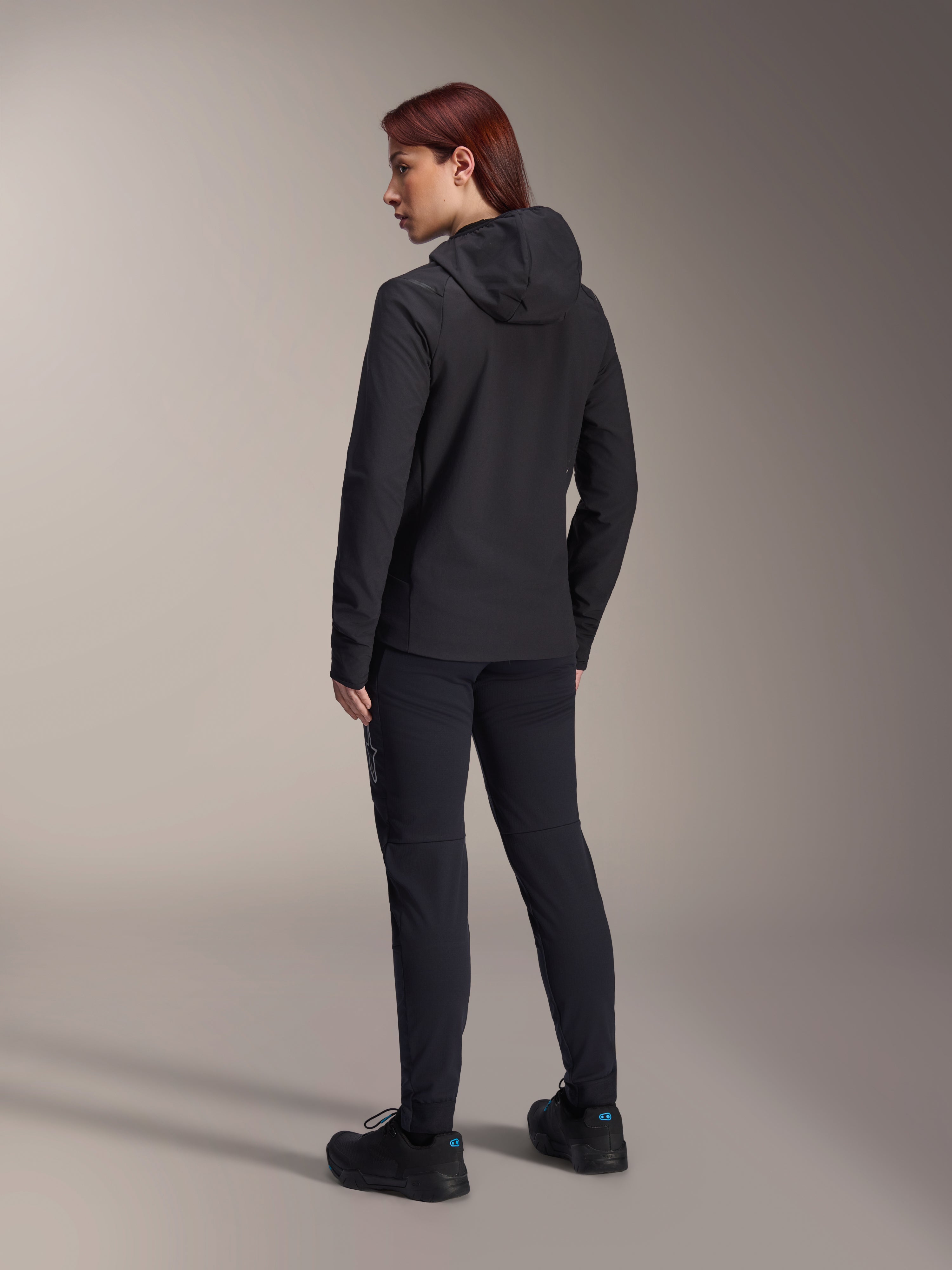 Alpinestars Stella A-Dura Thermal Jacket, damska kurtka rowerowa MTB, czarna, widok z tyłu podkreślający ocieplany kaptur i regularny krój, noszona z pasującymi czarnymi spodniami i butami, lekka izolacja termiczna do jazdy w zimne dni