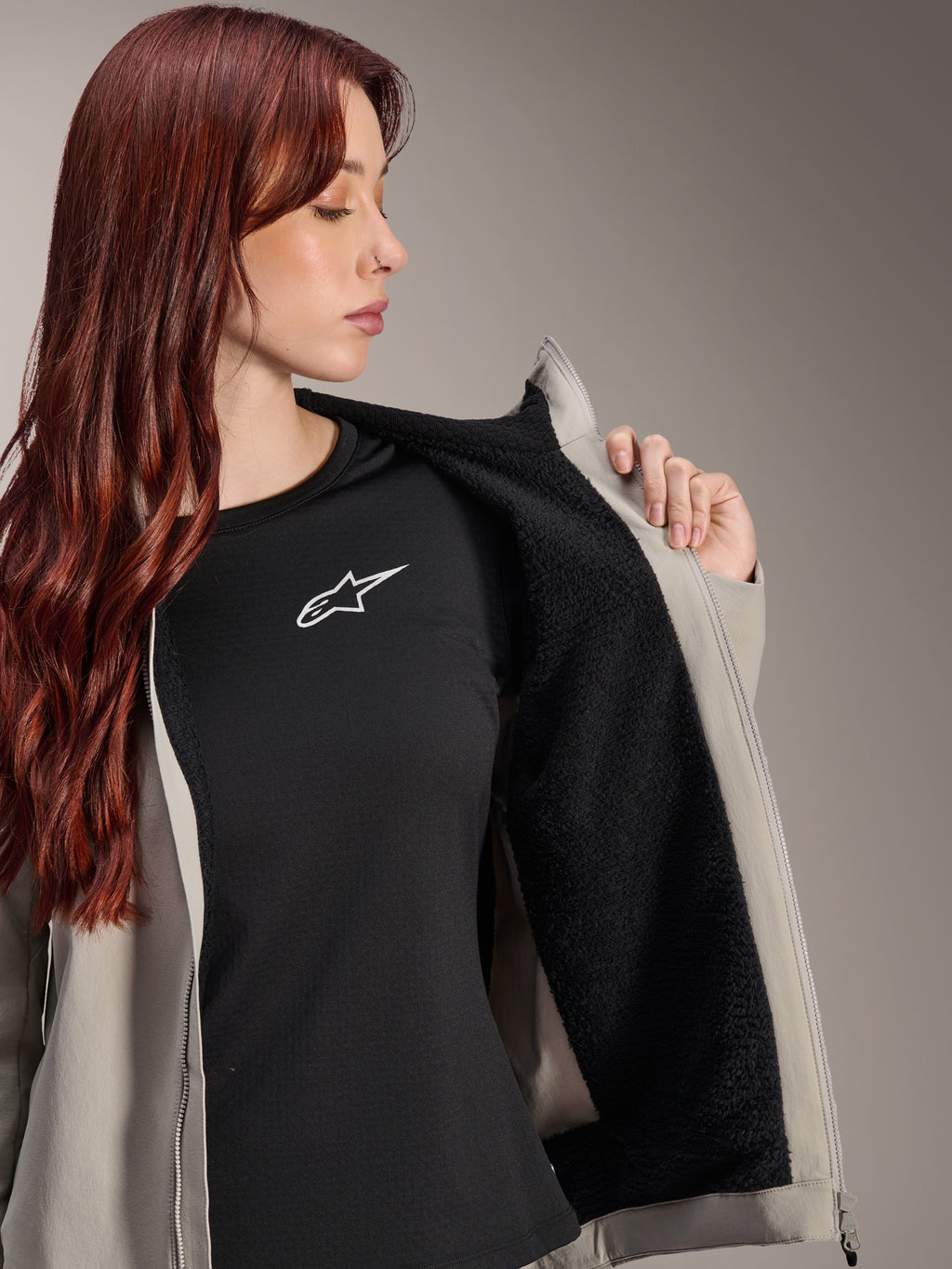 Kobieta w kurtce Alpinestars Stella A-Dura Thermal w kolorze Titanium, prezentująca czarną teksturowaną podszewkę z polaru, założona na czarny t-shirt z białym logo gwiazdy, lekka kurtka MTB na zimne dni.