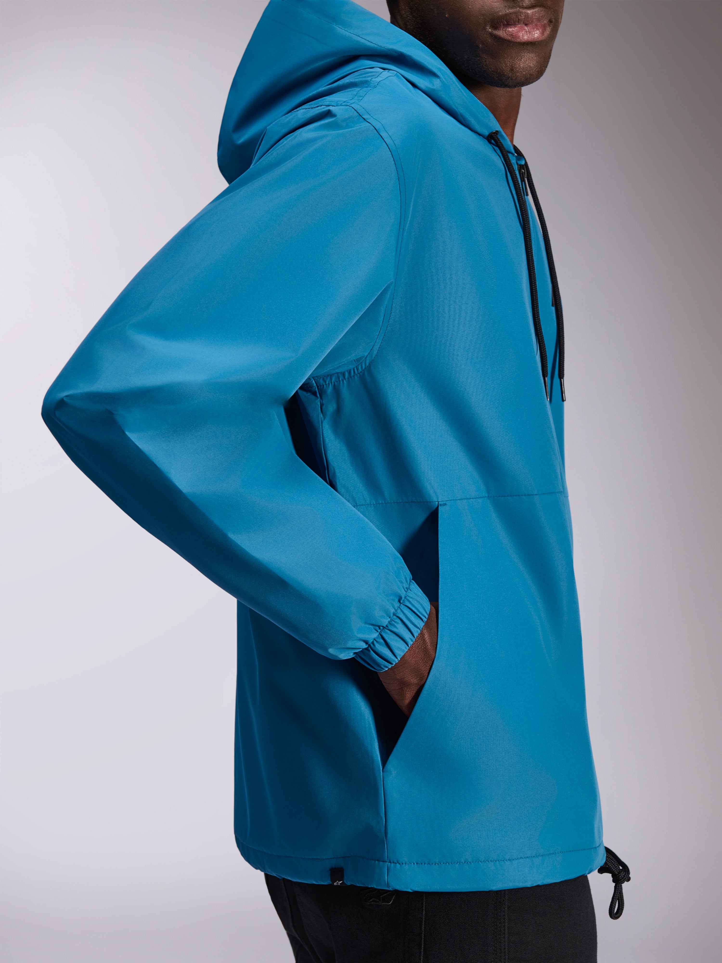 Alpinestars Speeder Chromium Windbreak Jacket, lekka wiatrówka z kapturem w kolorze niebieskim, widok z boku z elastycznymi mankietami i kieszeniami bocznymi, regulowany kaptur ze ściągaczami, swobodny design inspirowany sportami motorowymi