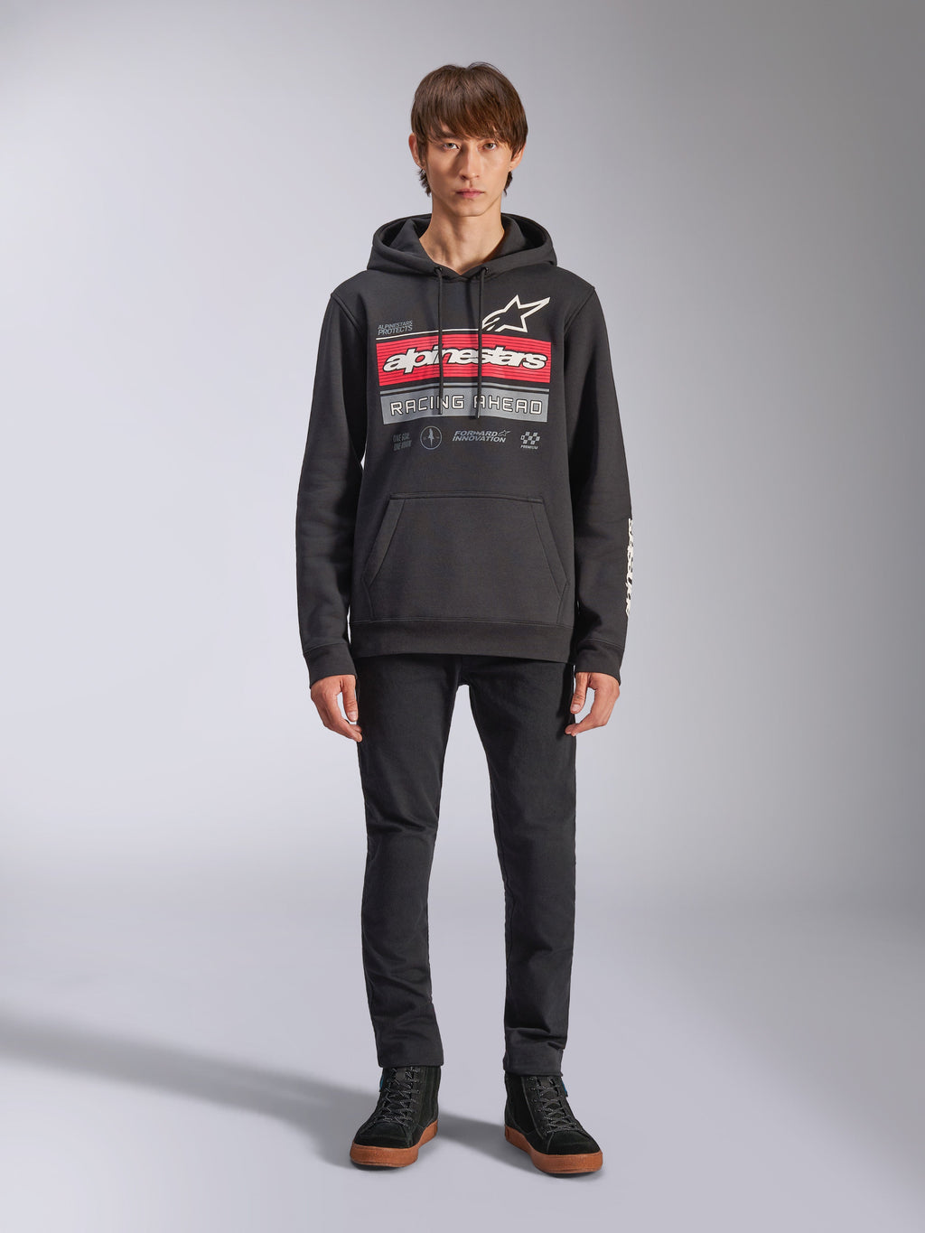 Alpinestars Harken Hoodie, czarna bluza z kapturem wkładana przez głowę, wyrazista grafika na piersi z czerwonymi pasami i napisem „Racing Ahead”, białe logo Astars, kieszeń kangurka, kaptur ze sznurkiem, codzienna odzież uliczna inspirowana sportami motorowymi