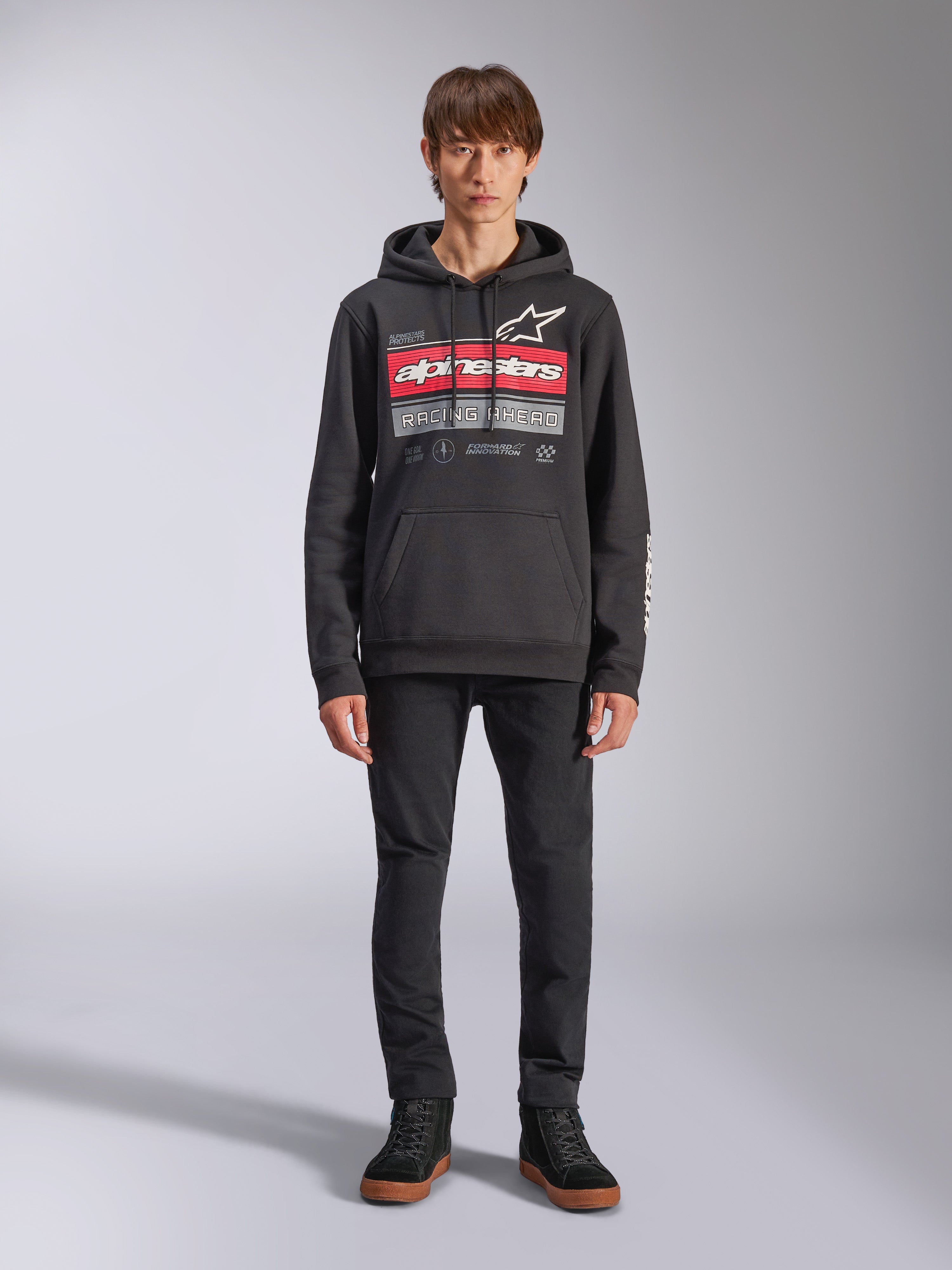 Alpinestars Harken Hoodie, czarna bluza z kapturem wkładana przez głowę, wyrazista grafika na piersi z czerwonymi pasami i napisem „Racing Ahead”, białe logo Astars, kieszeń kangurka, kaptur ze sznurkiem, codzienna odzież uliczna inspirowana sportami motorowymi