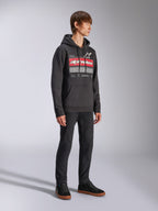 Alpinestars Harken Hoodie, czarna bluza polarowa z kapturem wkładana przez głowę, z dużą grafiką na piersi, czerwonym napisem Alpinestars i logo gwiazdy, kieszeń kangurka, noszona przez modela z czarnymi spodniami i sneakersami, casualowa odzież streetwearowa