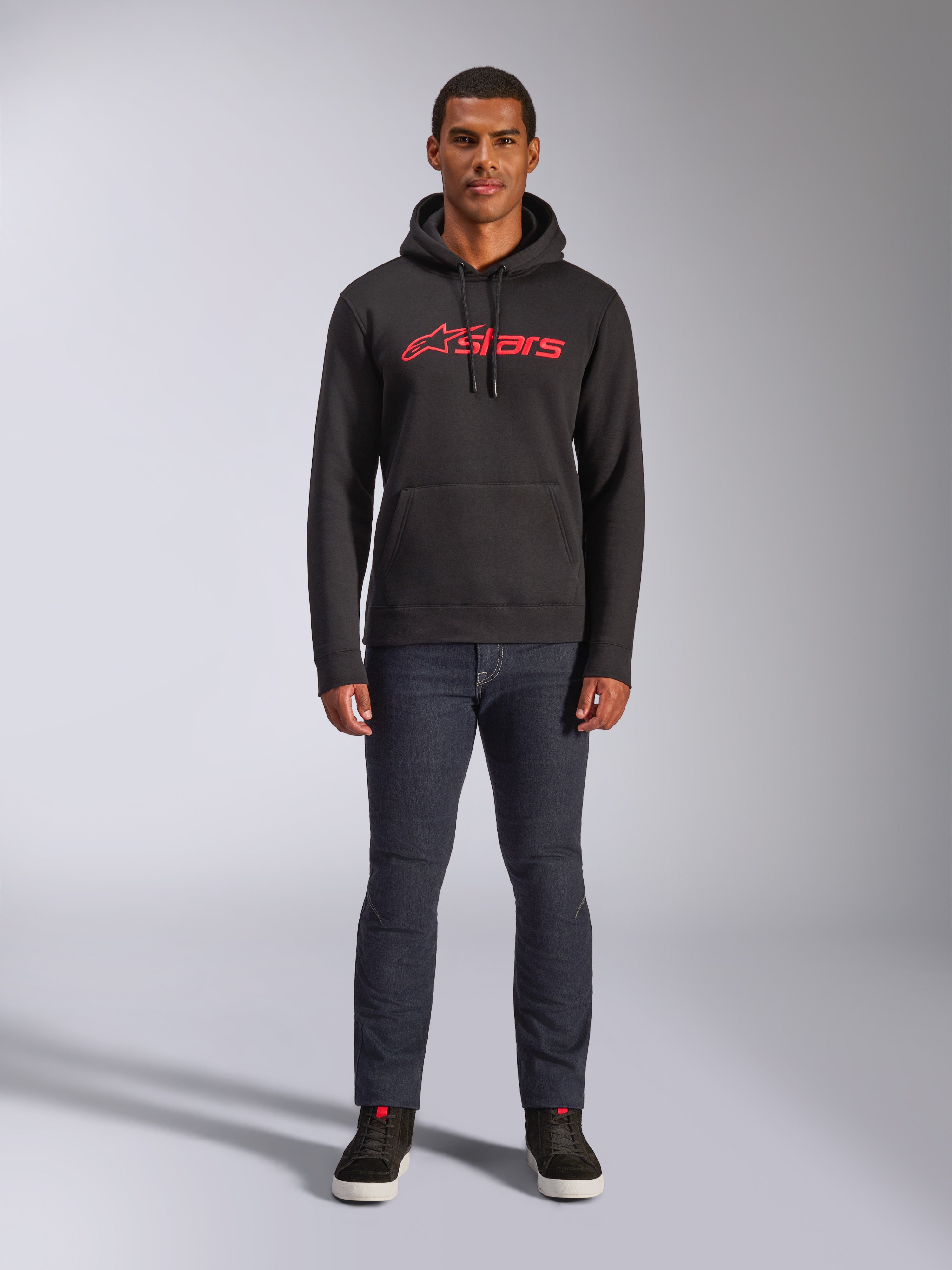 Alpinestars Blaze V3 Hoodie, casual streetwear, Black with Red Astars logo, front view, worn by model with dark denim pants and black sneakers, modern motorsport-inspired fleece design