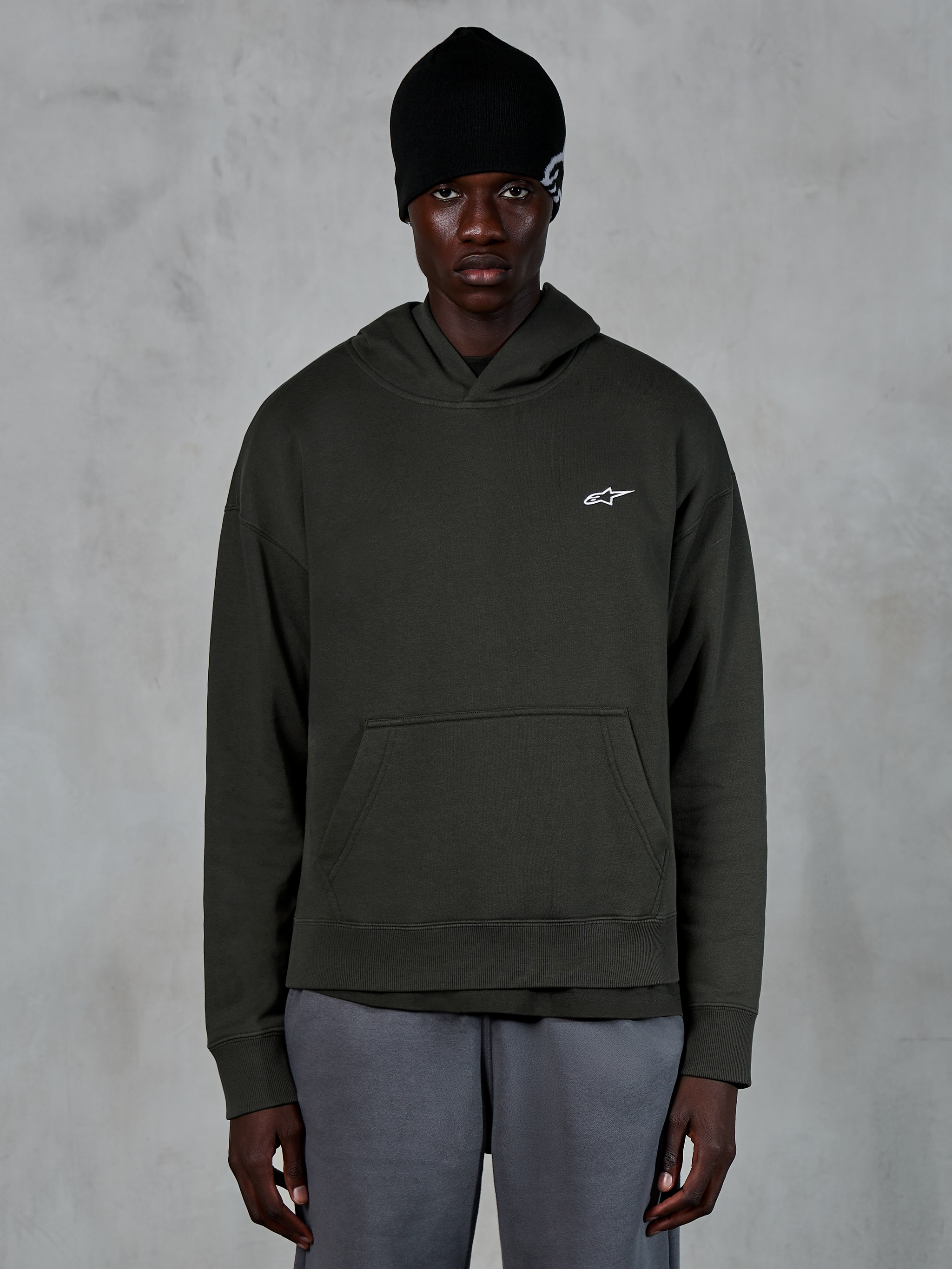 Alpinestars Essentials Ageless Hoodie, casual streetwear, Off Black pullover with a small white Alpinestars logo on the chest, worn with a black beanie, minimalist design with a front pouch pocket and stone-wash finish