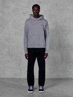 Alpinestars Essentials Ageless Hoodie, Silver, male model wearing casual streetwear, small black Alpinestars logo on chest, front kangaroo pocket, minimalist design, paired with black pants and sneakers.