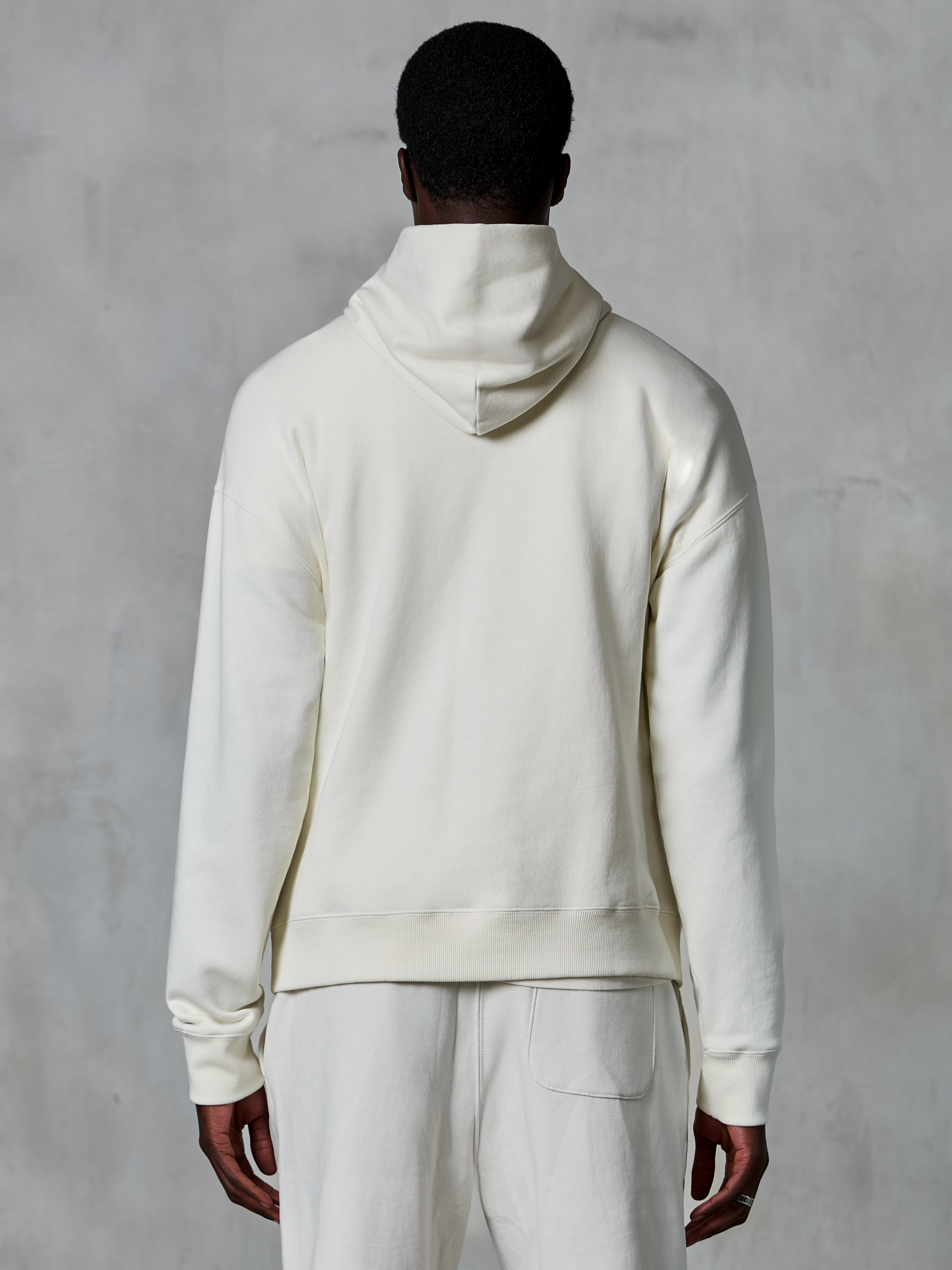 Alpinestars Essentials Ageless Hoodie, kremowa bluza z kapturem typu pullover, widok z tyłu na modelu, czysty minimalistyczny design, pasujące spodnie codzienne, luźny krój zapewniający codzienny komfort