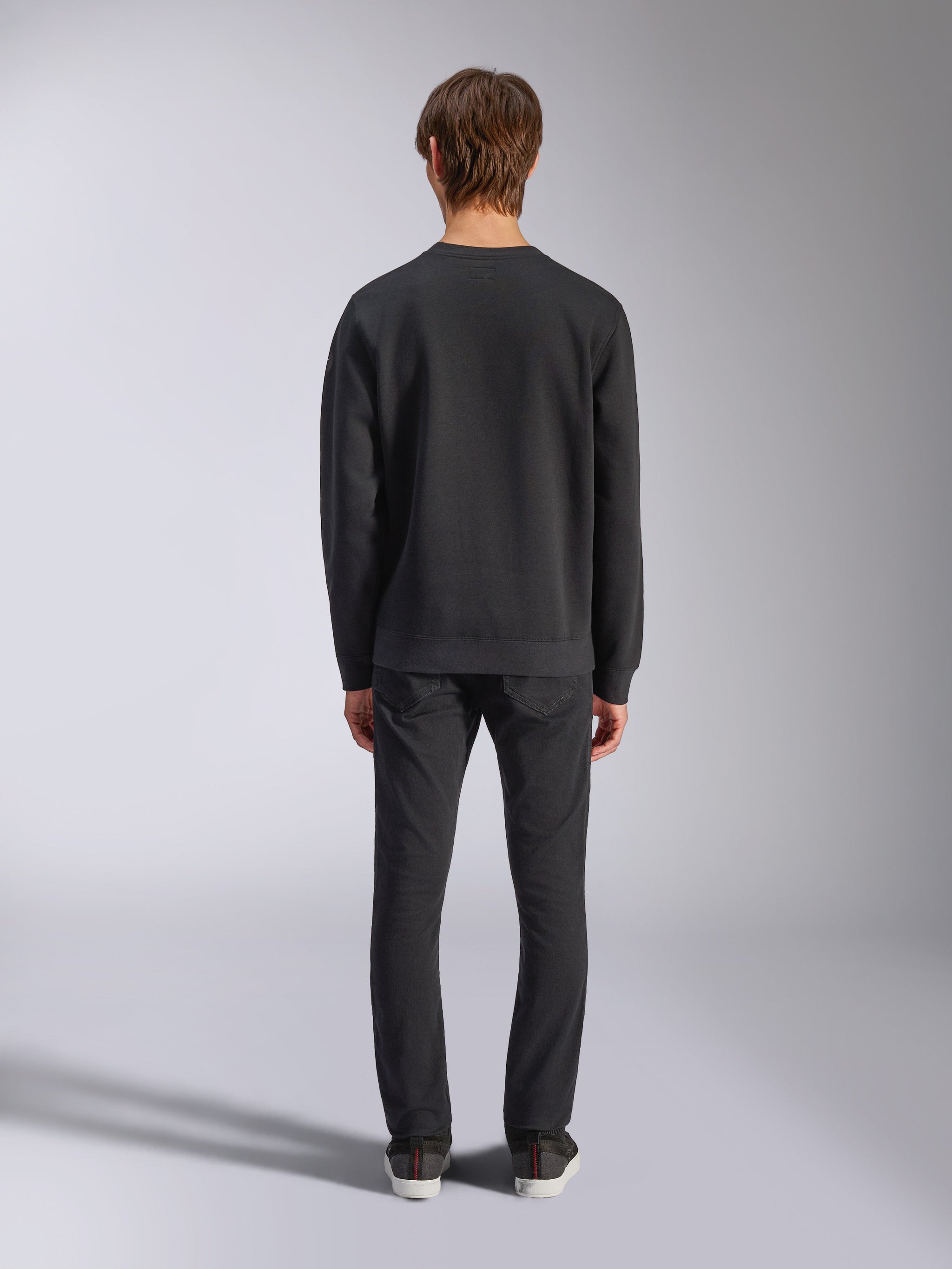 Alpinestars Bettern Crew, czarna bluza typu crewneck, widok z tyłu na modelu, ściągacz przy kołnierzu i na dole, codzienna odzież uliczna inspirowana sportami motorowymi