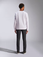Alpinestars Bettern Crew, biała bluza typu crewneck, widok z tyłu na modelu, zestawiona z ciemnymi jeansami i sneakersami, casualowa odzież uliczna inspirowana sportami motorowymi