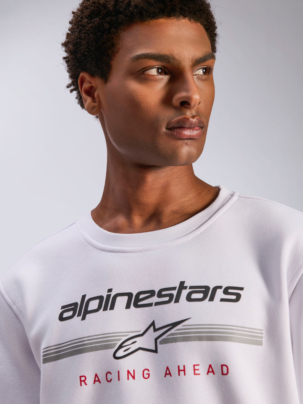 Alpinestars Bettern Crew, biała bluza typu crewneck z polaru, czarne logo Alpinestars z szarymi poziomymi liniami i czerwonym napisem „Racing Ahead”, codzienna odzież streetwearowa inspirowana sportami motorowymi