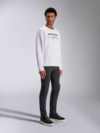 Alpinestars Bettern Crew, biała bluza typu crewneck z czarnym logo Alpinestars i czerwonym napisem „Racing Ahead”, casualowa odzież inspirowana motorsportem, prezentowana przez modela w ciemnych spodniach i czarnych sneakersach