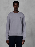 Alpinestars Essentials Ageless Crew, Silver crewneck sweatshirt worn by a model, featuring a small black star logo on the chest, relaxed fit with ribbed cuffs and hem, casual motorsport streetwear